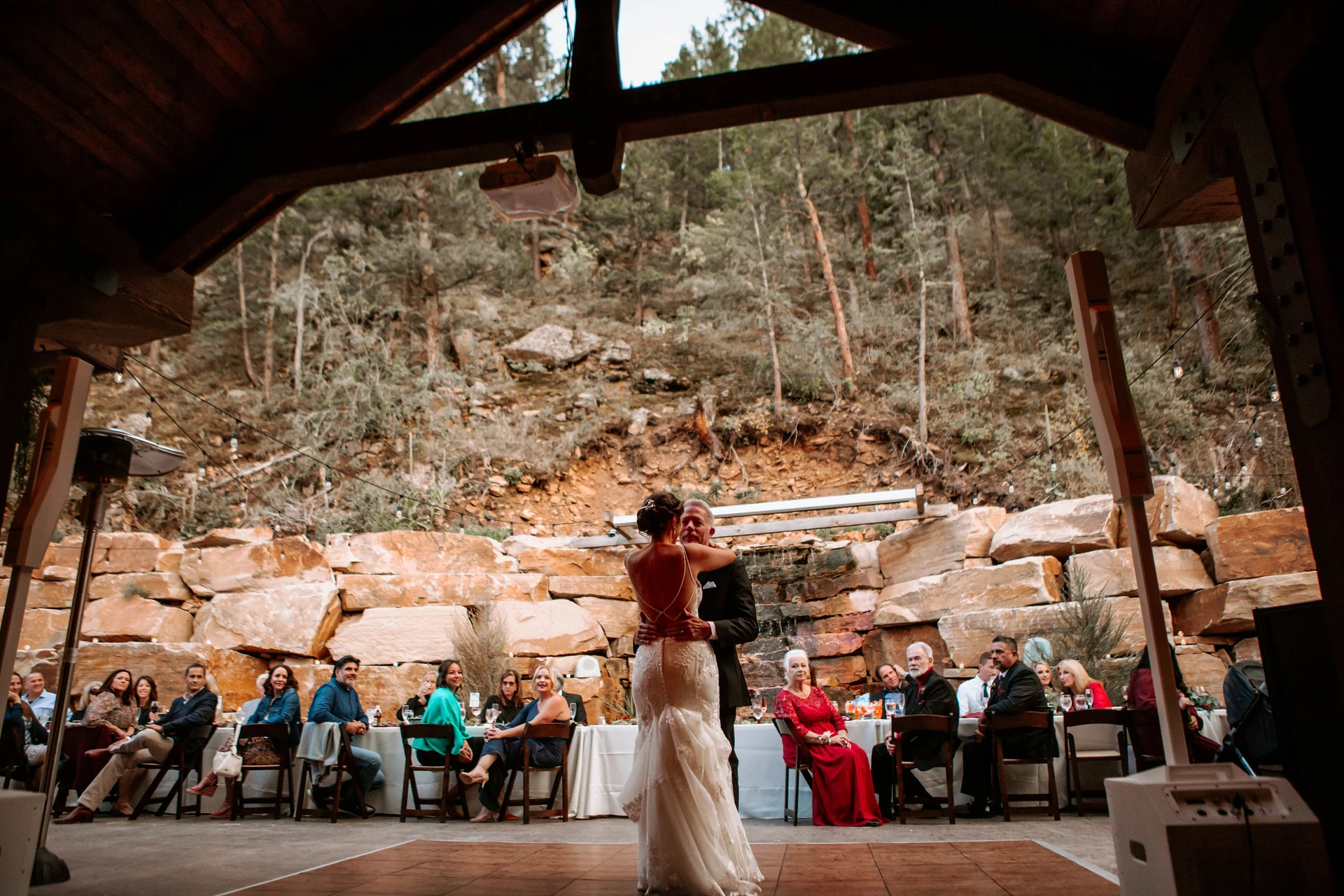 A wedding couple sharing their first dance beneath a timber pavilion, surrounded by guests