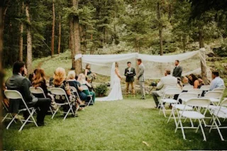 Guests watching an outdoor wedding ceremony beneath a white-draped arch