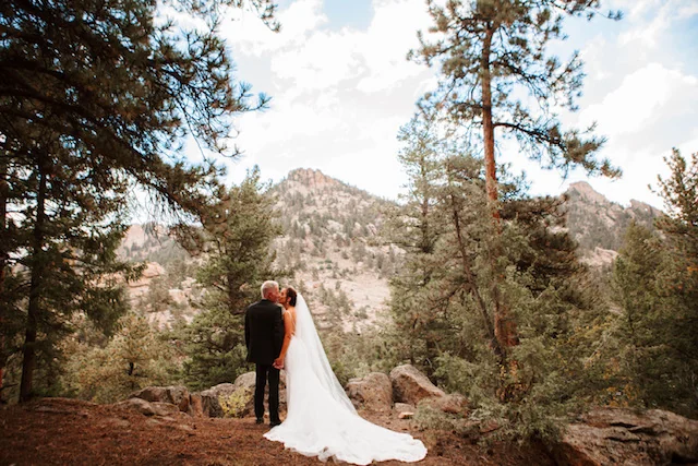 A wedding couple among pine trees with a mountain backdrop