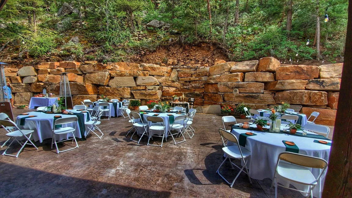 An outdoor reception patio with round tables, white linens, green runners, and a stone waterfall